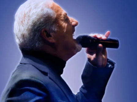 A person singing passionately on stage against a vibrant blue backdrop.
