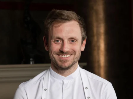 A happy chef smiling warmly in a stylish hotel setting.