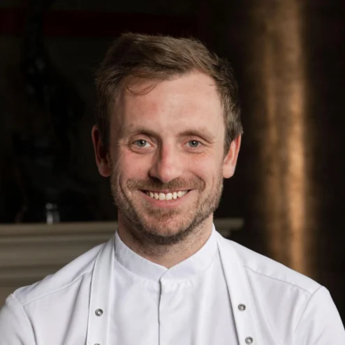 A happy chef smiling warmly in a stylish hotel setting.