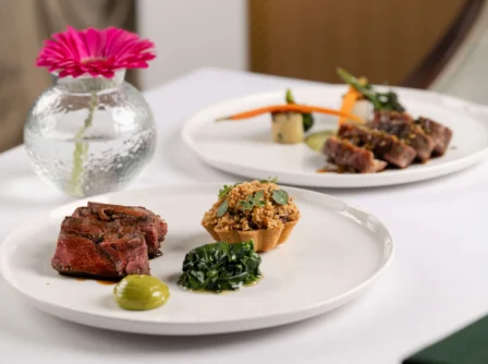 Elegant dining table set with gourmet meals and a vibrant pink flower in a vase.