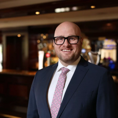 Smiling man in suit at hotel bar setting, creating a warm and welcoming atmosphere.