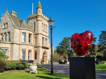 Family enjoying a sunny day outside a historic hotel with lush gardens and large heart sculpture.