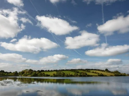 Scenic view of lush hills and tranquil lake under a bright blue sky with fluffy clouds.