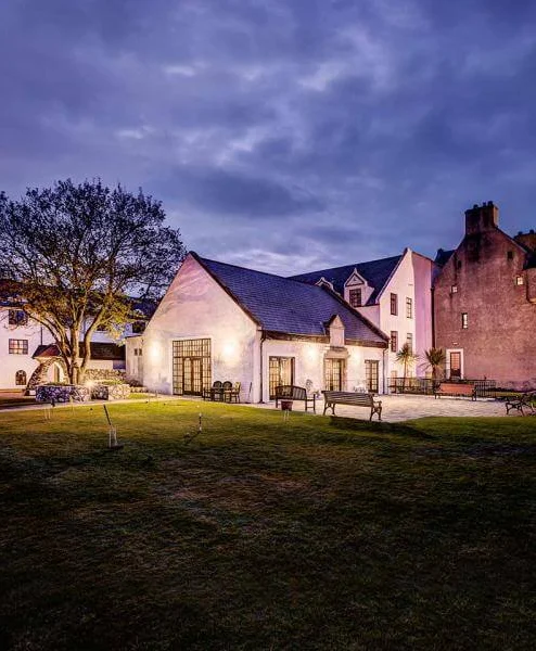 A cosy evening view of a historic Hastings Hotel with warm lights illuminating the garden.