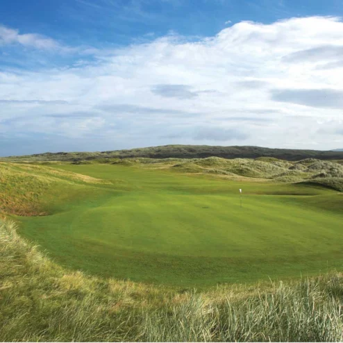 Scenic golf course amid rolling green dunes under a blue sky at Hastings Hotels.