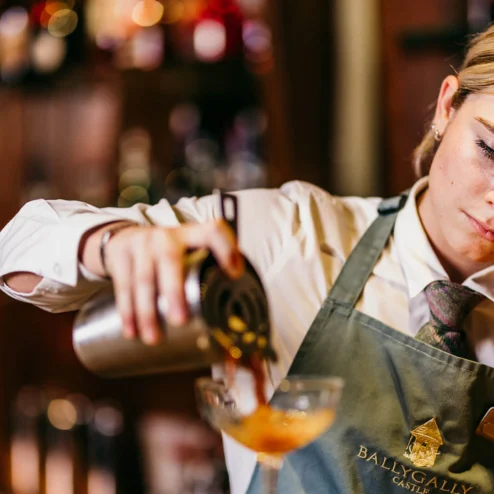 A bartender at Ballygally Castle pours a cocktail, creating an elegant drink at the bar.