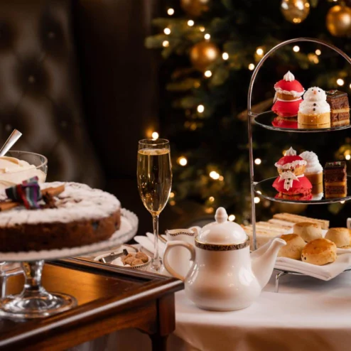 Festive afternoon tea with cakes and champagne by a decorated Christmas tree.