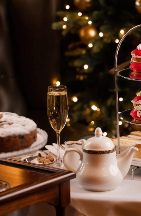 Festive afternoon tea with cakes and champagne by a decorated Christmas tree.