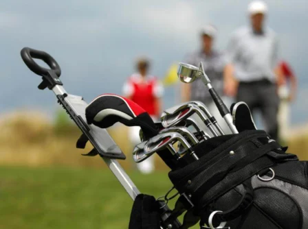 Close-up of golf clubs with a family playing golf in the background.