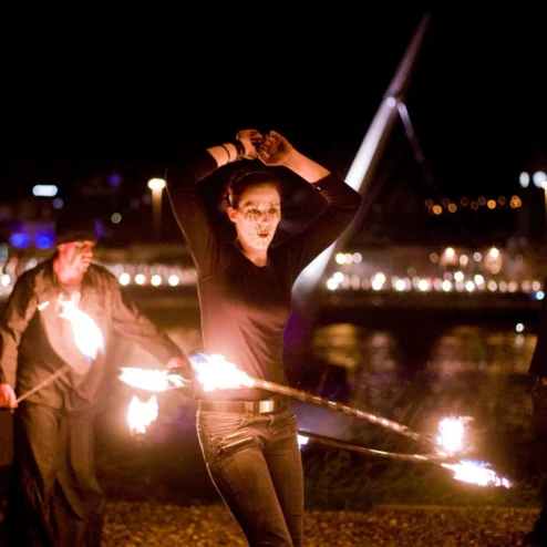 Family enjoying outdoor fire show near a lit bridge at night in Hastings.