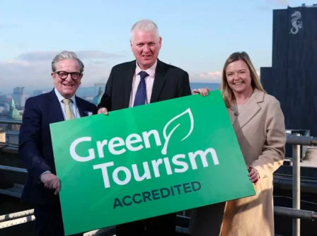 A cheerful group proudly displays a "Green Tourism Accredited" sign on a rooftop.