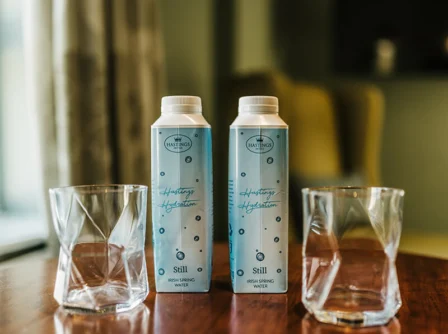 Hastings Hotels bottled water and glasses on a wooden table in a cosy room.