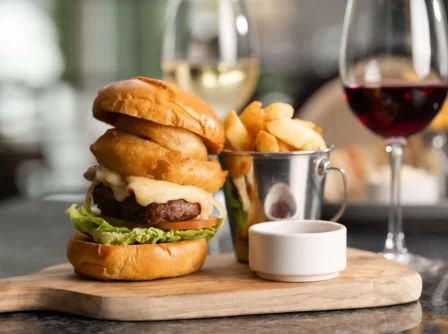 Delicious gourmet burger with onion rings and wine in an inviting restaurant setting.