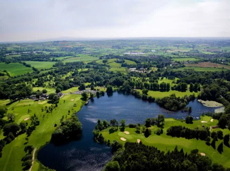 Aerial view of lush green landscapes, serene lake, and a sprawling golf course at Hastings Hotels.