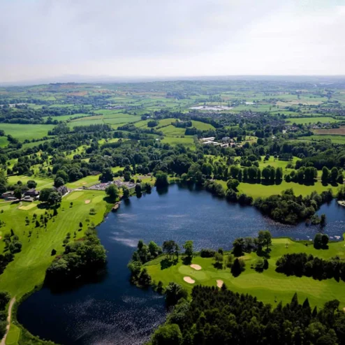 Aerial view of lush green landscapes, serene lake, and a sprawling golf course at Hastings Hotels.