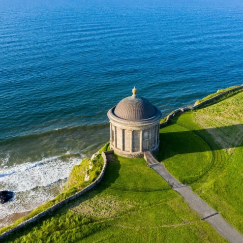 Iconic Mussenden Temple overlooking the vast blue sea and lush green cliffs.
