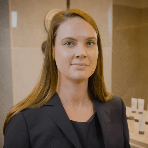 A friendly hotel staff member in a well-lit bathroom with elegant toiletries.