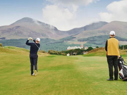 A couple enjoy a scenic golf game at a lush, mountainous resort.