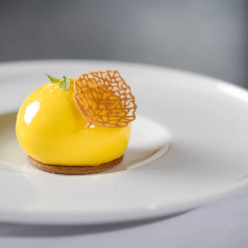 Elegant dessert on a white plate at Hastings Hotels, featuring a glossy yellow mousse.