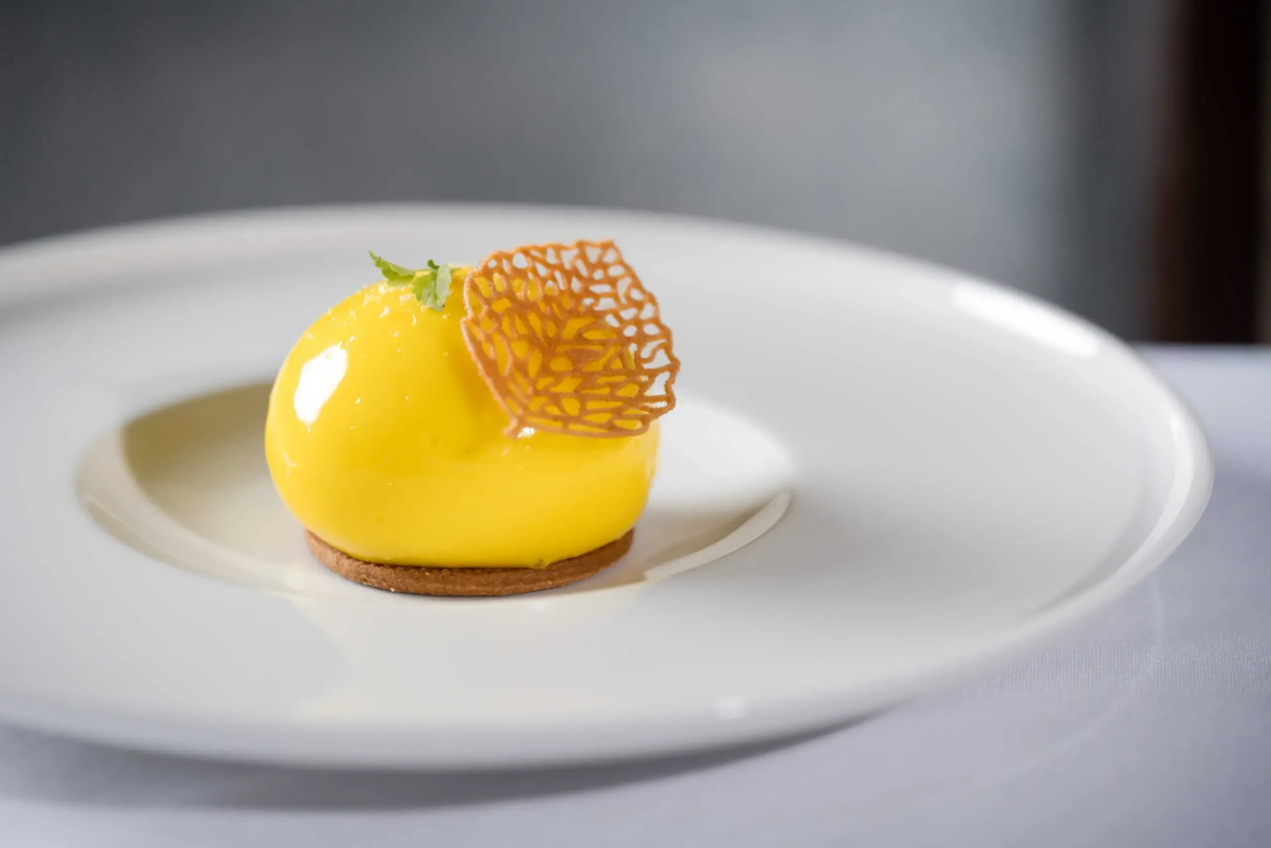 Elegant dessert on a white plate at Hastings Hotels, featuring a glossy yellow mousse.