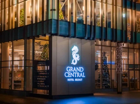 Illuminated entrance of Grand Central Hotel Belfast at night, decorated with lights.