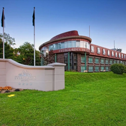 The Everglades Hotel exterior with flags, surrounded by lush green gardens at dusk.