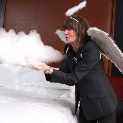 Woman dressed as an angel prepares bed in a cosy hotel room.