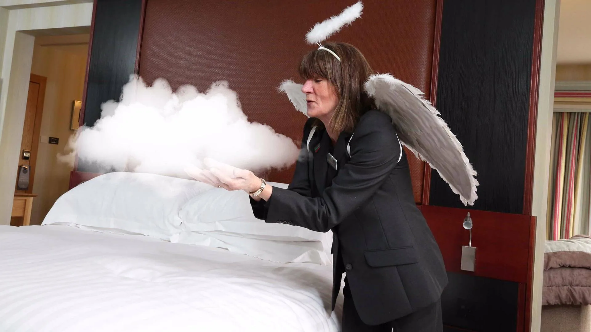 Woman dressed as an angel prepares bed in a cosy hotel room.