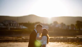 A couple embracing at sunset on a serene beach near Hastings Hotel.