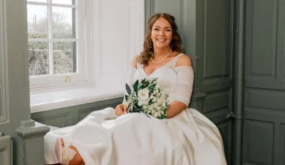 Bride smiling by a window, holding a bouquet in an elegant hotel setting.