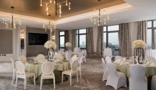 Elegant hotel ballroom set for a formal event with round tables and floral centrepieces.