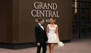 A couple in formal attire smile warmly outside Grand Central Hotel Belfast.