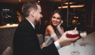 Couple enjoying cocktails, dressed elegantly, in a cosy, dimly lit hotel bar.
