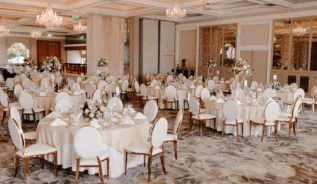 Elegant hotel ballroom set for a family wedding reception, with round tables and chandeliers.
