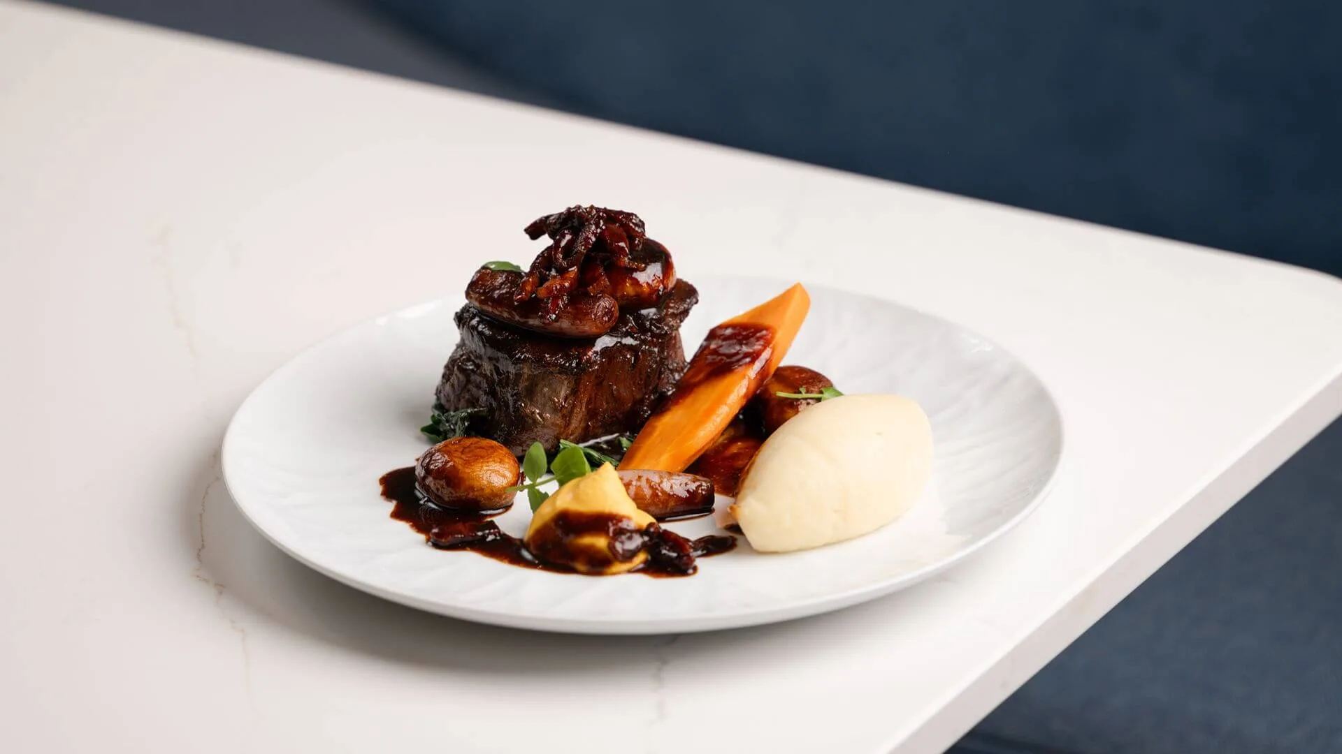 Succulent braised beef with glazed carrots, baby onions and creamy mash on a white plate in a hotel restaurant (no visible text)