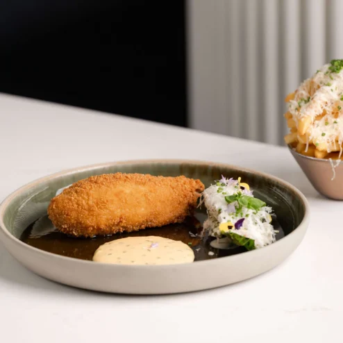 Crispy croquette with sauce and salad beside loaded fries on a table.
