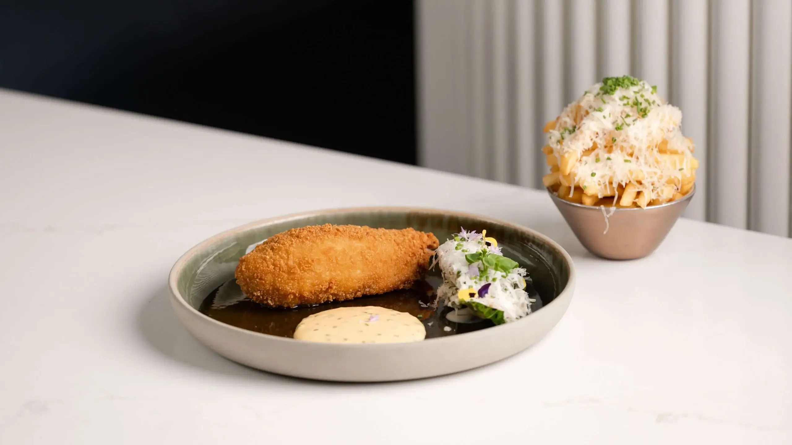 Crispy croquette with sauce and salad beside loaded fries on a table.